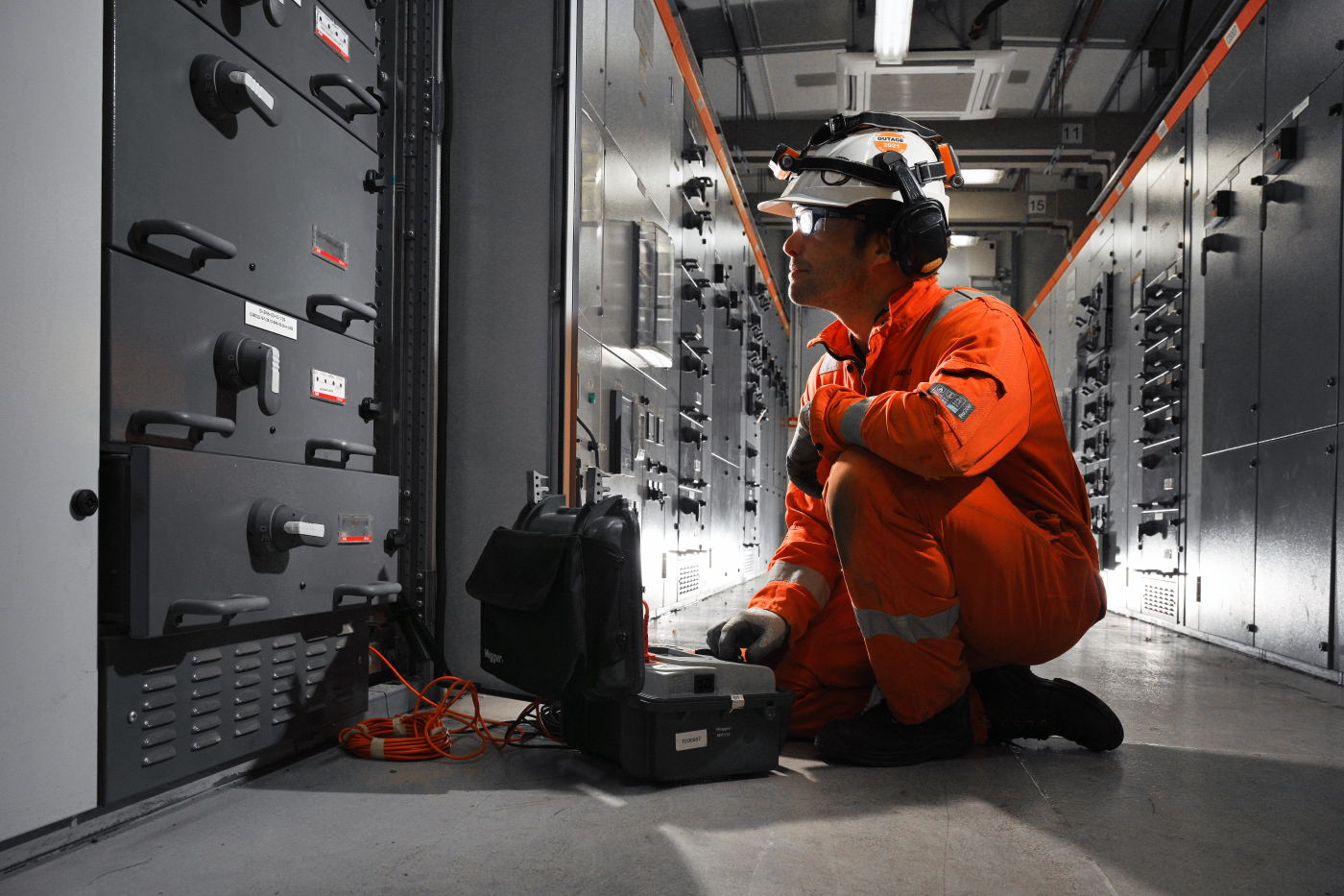 Engineer in orange kneeling by grey panel